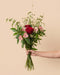Eine Hand hält den Ich-liebe-Dich-Strauss mit einer roten Rose, rosa Alstroemerien, weissem Schleierkraut und grünen Gräsern vor einem warmen beigen Hintergrund.