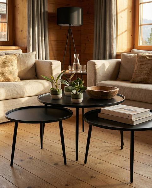 Ein gemütliches Wohnzimmer mit beigen Sofas, neutralen Kissen, Holzwänden und drei schwarzen Couchtischen mit den Schweizer Überraschungs-Babypflanzen (3er-Set), Büchern, einer Holzschale und einer Glaskaraffe. Sonnenlicht strömt durch große Fenster.