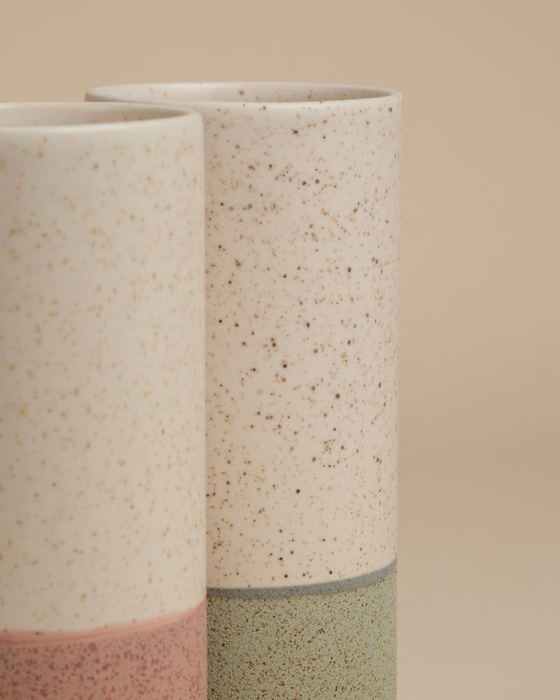 Die feey Keramik-Vase (Variado | 21 cm) hat ein cremefarben gesprenkeltes Oberteil in Grün und Rosa, inspiriert von klaren Designlinien. Vor einem beigen Hintergrund ist sie ideal für die Präsentation von Zimmerpflanzen oder als einzigartige Blumenvase.