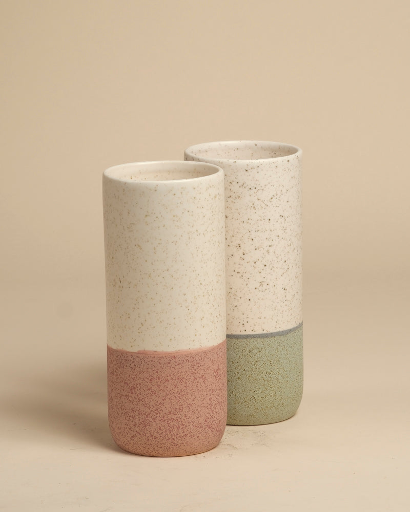 Zwei Keramik-Vasen (Variado | 21 cm), eine mit gesprenkeltem Creme und gedämpftem Rosa, die andere mit Creme und gedämpftem Grün. Ideal als Blumenvase für Zimmerpflanzen, ausgestellt auf einer beigen Oberfläche mit einem passenden Hintergrund.