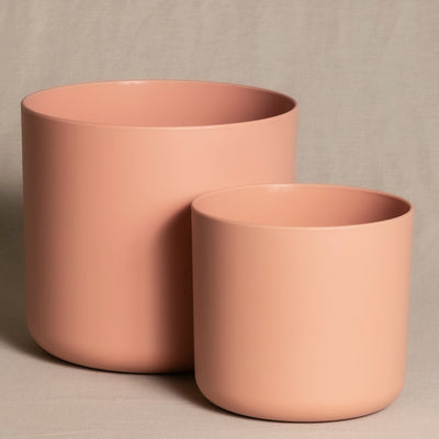Zwei minimalistische, runde, mattrosa Topfsets (18, 14) stehen auf einer neutralen Stoffoberfläche. Der größere Topf steht etwas links hinter dem kleineren, wodurch ein optisch ansprechendes Arrangement entsteht.