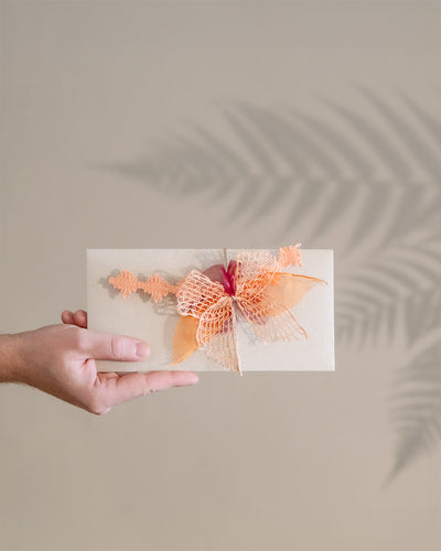 Gutscheinumschlag mit orangener Schleife wird von links von einer Hand ins Bild gehalten.