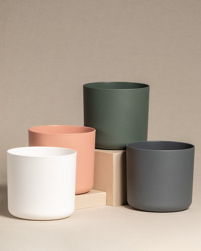 Pflanznübertöpfe in den Farben weiss, grün, pink und anthrazit stehen auf einem Holztisch