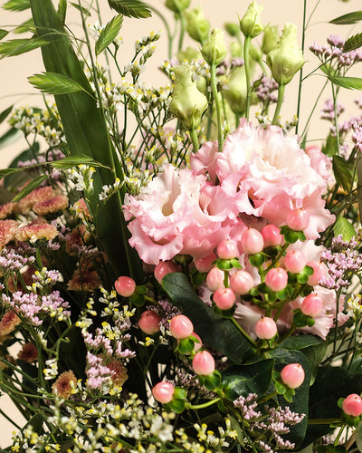 Morgenlicht" ist ein von Hand gebundener Blumenstrauß mit pinken Lisianthus, pinkem Hypericum, grünen Blättern sowie zarten lila und weißen Herbstblumen - perfekt für Ihr Zuhause vor hellem Hintergrund.