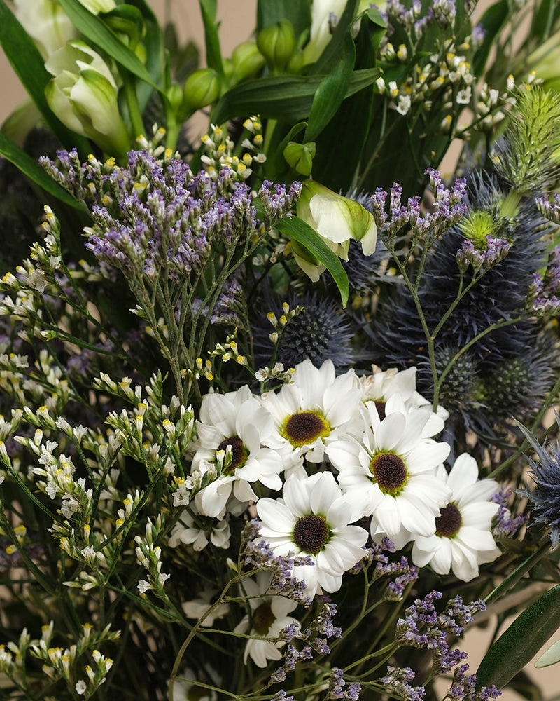 Der Strauß "Nebelmeer" kombiniert weiße Gänseblümchen, violette Statice, blaue Disteln und frisches Blattgrün zu einem Arrangement voller zarter Blüten und erfrischender Leichtigkeit.