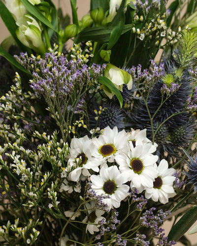 Der Strauß "Nebelmeer" kombiniert weiße Gänseblümchen, violette Statice, blaue Disteln und frisches Blattgrün zu einem Arrangement voller zarter Blüten und erfrischender Leichtigkeit.