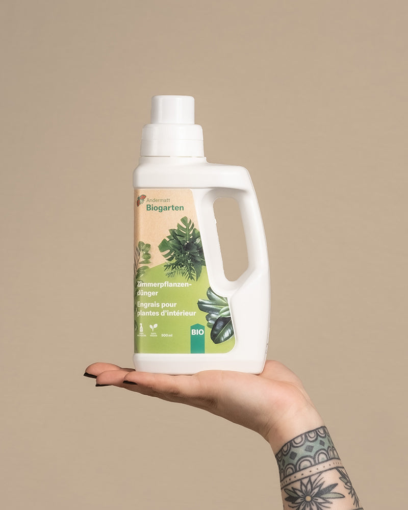 Hand balanciert eine Flasche mit Flüssigdünger für Zimmerpflanzen