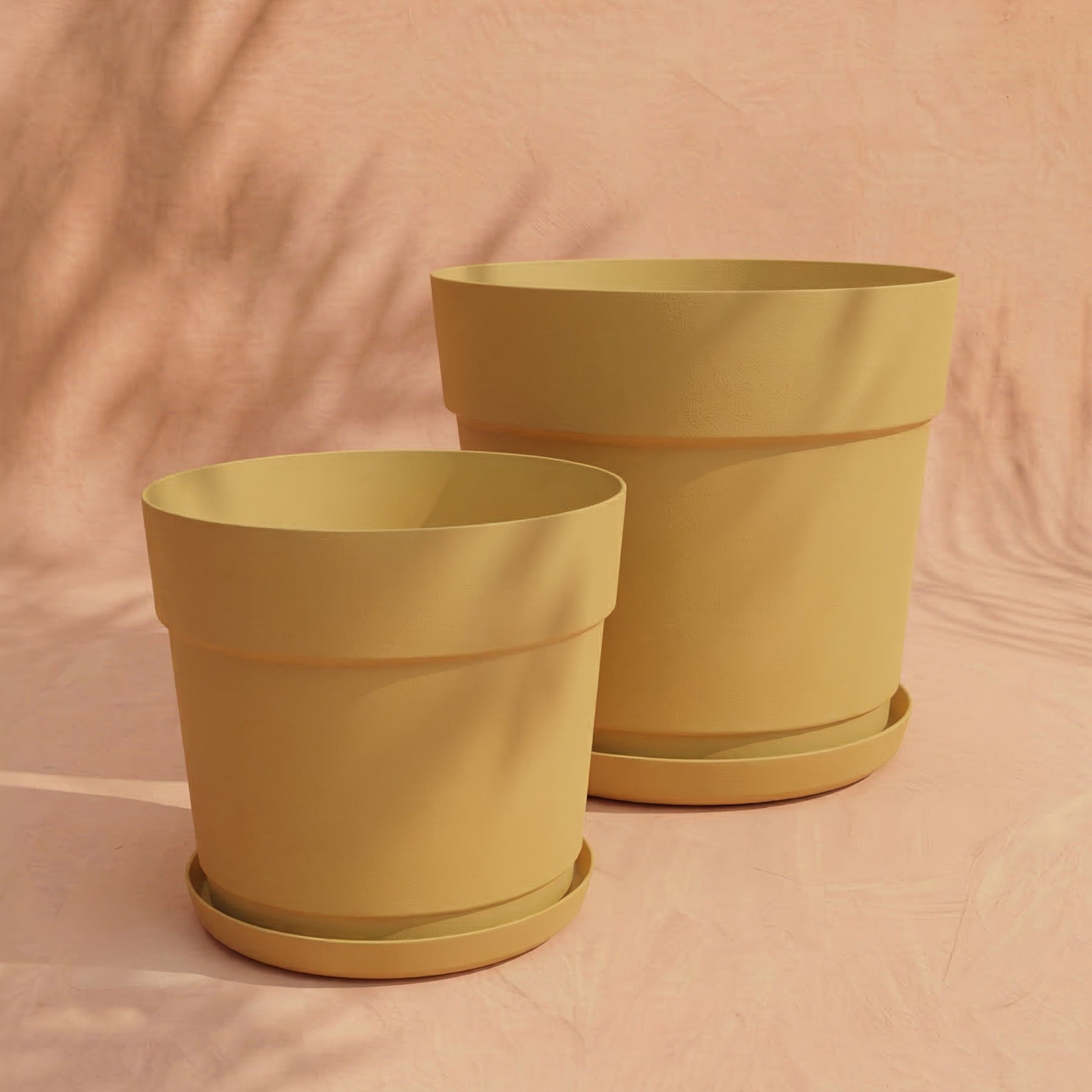 Das Pflanzkübel-Set 'Bloom' (38, 29) aus recyceltem Kunststoff mit Untersetzern steht stilvoll nebeneinander auf pfirsichfarbener Fläche - UV-beständig und umweltfreundlich.