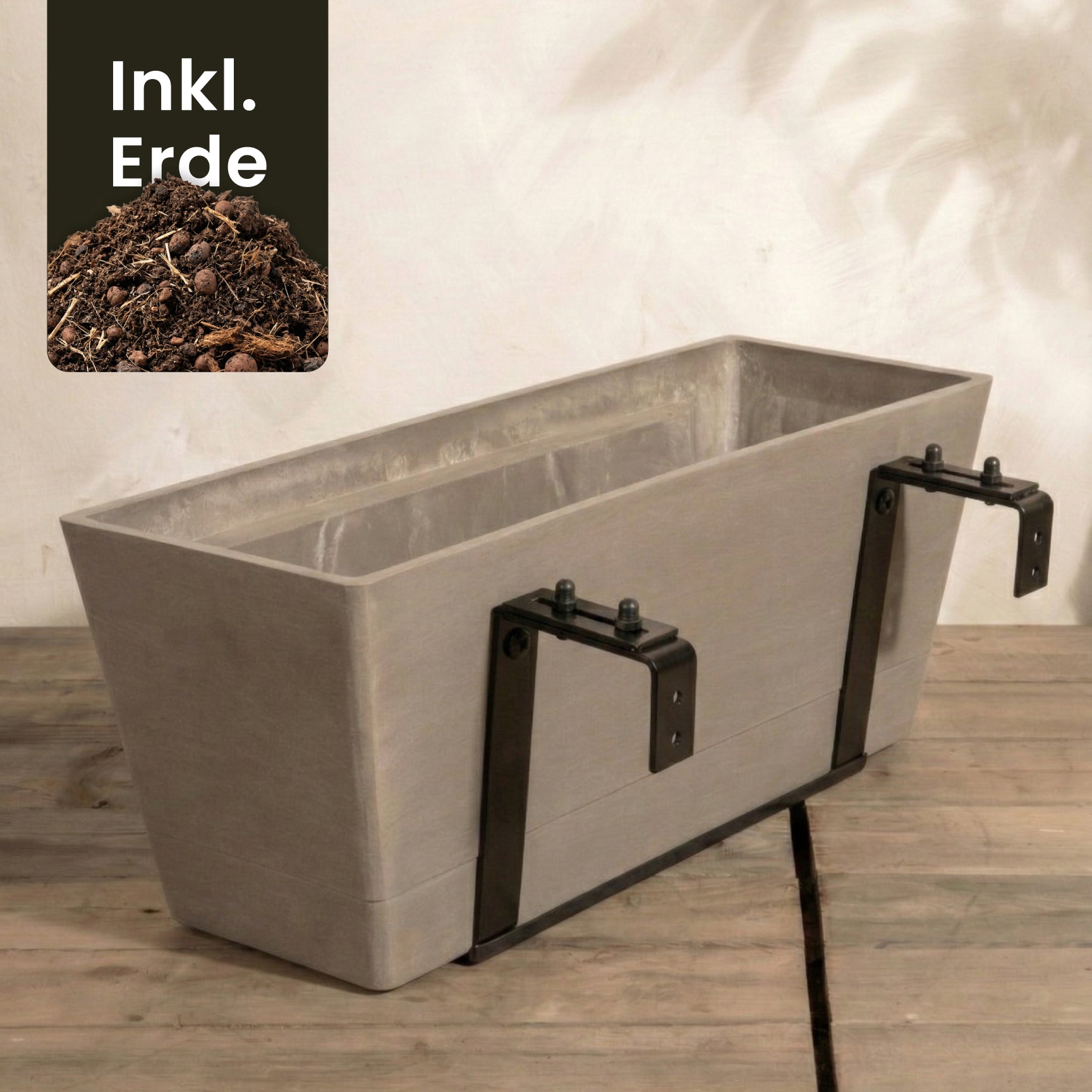 Rechteckiger beiger Pflanzkasten für Geländer (Brügge | 48 cm) mit schwarzen Metallklammern für ein Hängesystem Balkon, auf Holz gestellt. Oben links im Bild ist Erde und der Text 