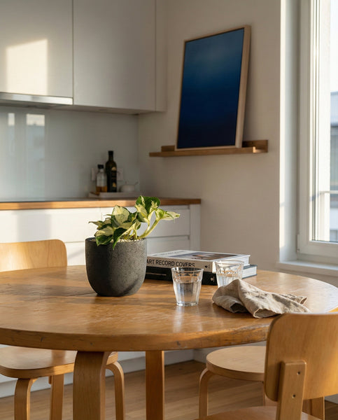 In einer sonnenbeschienenen Küche steht ein runder Esstisch aus Holz mit einem Efeutute 