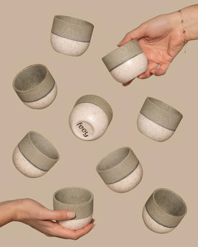 Hände halten Keramikbecher mit gesprenkeltem Design aus dem Keramik Baby-Topfset „Variado“ (9 Stk.). Ein Becher ist umgedreht, sodass das „freey“-Logo am Boden sichtbar ist und an Lieblingsfarbe erinnert. Der neutrale beige Hintergrund unterstreicht die subtile Schönheit dieser einzigartigen Kreationen.