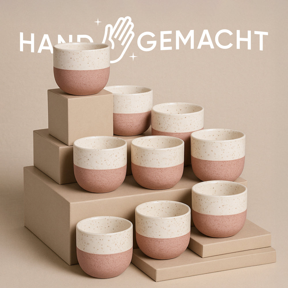 Das Keramik-Baby-Topfset „Variado“ (9 Stk.) besteht aus gesprenkelten Keramikbechern mit rosa Boden und cremefarbenem Deckel, arrangiert auf beigen Boxen mit zarter Babypflanze. „HANDGEMACHT“ und ein Handsymbol im Hintergrund symbolisieren die Verbindung von Natur und Handwerk.