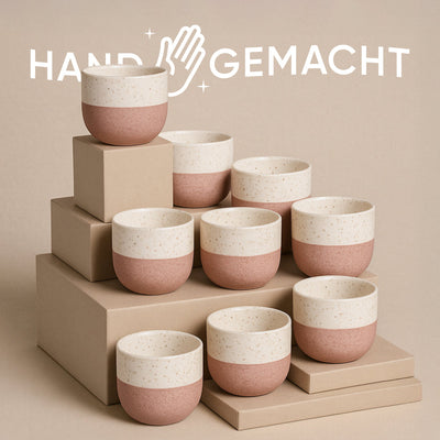 Das Keramik-Baby-Topfset „Variado“ (9 Stk.) besteht aus gesprenkelten Keramikbechern mit rosa Boden und cremefarbenem Deckel, arrangiert auf beigen Boxen mit zarter Babypflanze. „HANDGEMACHT“ und ein Handsymbol im Hintergrund symbolisieren die Verbindung von Natur und Handwerk.