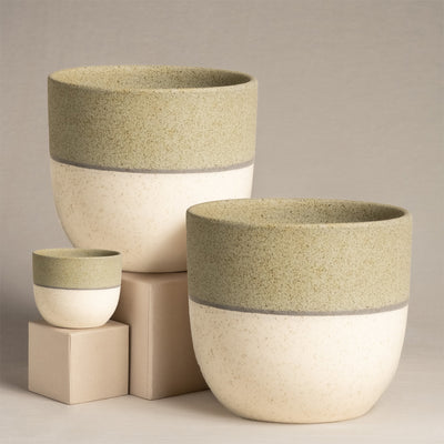 Das Keramik-Topfset „Variado“ (2 × 18, 7) besteht aus drei handgefertigten Keramiktöpfen in zweifarbigem Design mit einer erdigen grünen Oberseite und einer gesprenkelten cremefarbenen Unterseite, angeordnet auf beigen Würfeln vor einem neutralen Hintergrund.