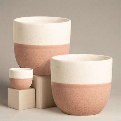Das Keramik-Topfset „Variado“ (2 × 18, 7) besteht aus vier handgefertigten Keramiktöpfen in verschiedenen Größen mit einem gesprenkelten zweifarbigen Design – oben cremefarben und unten staubig-rosa –, die sich wunderschön vor einem neutralen Hintergrund auf beigen Würfeln präsentieren.