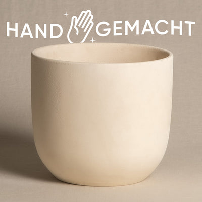 Ein glatter, cremeweißer, heller Keramik-Topf (Direito | 18 cm ⌀) steht zentriert auf einem beigen Untergrund. Oberhalb des Topfes ist ein stilisiertes Logo mit einer abgebildeten Hand und funkelndem Text „HAND GEMACHT“ zu sehen.
