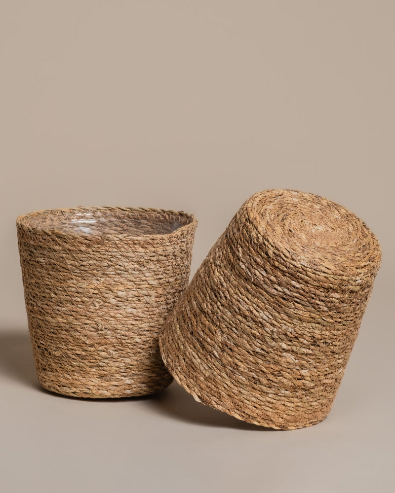 Zwei runde Pflanzkörbe aus Seegras (Kesat | 18 cm ⌀) sind auf neutralem Hintergrund zu sehen: Einer steht aufrecht, der andere lehnt seitlich an ihm.