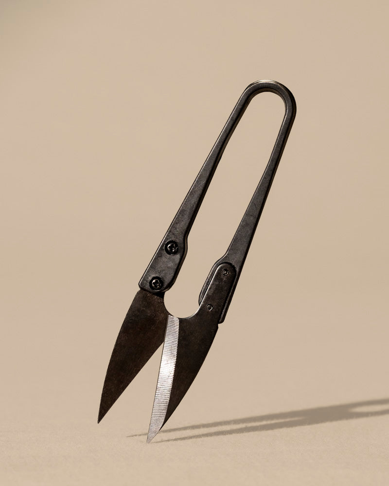 Die Kleine Pflanzenschere, eine kleine Metallschere im Vintage-Stil mit scharfen, spitzen Klingen, die an klassische Bonsai-Scheren erinnern, steht aufrecht auf einem neutralen beigen Hintergrund und wirft einen weichen Schatten.