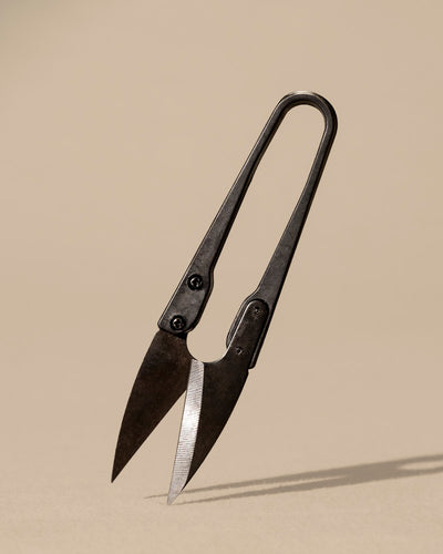 Die Kleine Pflanzenschere, eine kleine Metallschere im Vintage-Stil mit scharfen, spitzen Klingen, die an klassische Bonsai-Scheren erinnern, steht aufrecht auf einem neutralen beigen Hintergrund und wirft einen weichen Schatten.