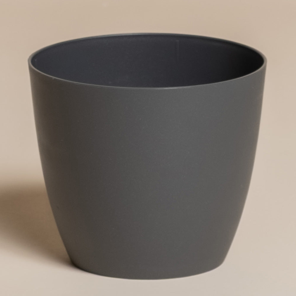 Der Kunststoff-Topf (Kiki | 11 cm Ø) ist ein schlichter, dunkelgrauer, zylindrischer Topf mit einer glatten, matten Oberfläche, der ideal ist, um Ihre Pflanzen in Szene zu setzen und Ihrem Zuhause einen modernen Touch zu verleihen. Fotografiert auf einem hellbeigen Hintergrund.