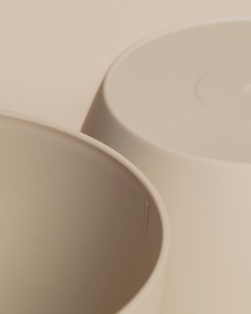 Nahaufnahme von zwei beigen Kunststoff-Töpfen (Kiki | 11 cm Ø), einer aufrecht und einer verkehrt herum, mit glattem, minimalistischem Design - ideal, um ein Pflänzchen in Ihrem Zuhause vor einem neutralen Hintergrund zu präsentieren.