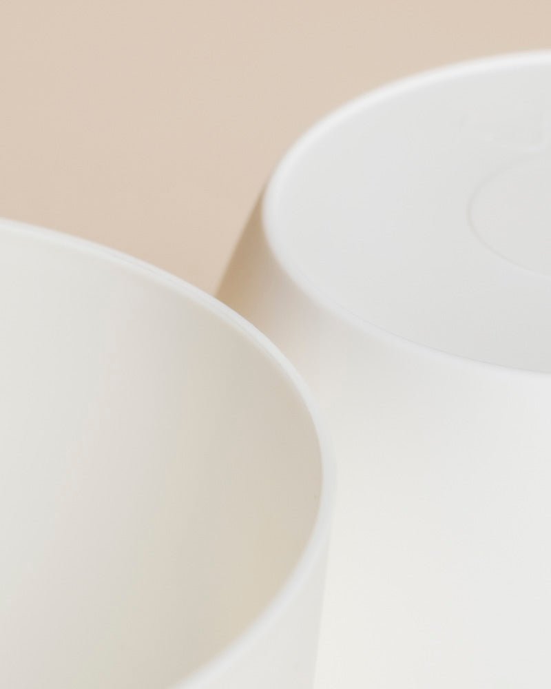 Nahaufnahme zweier weißer, glatter Kunststoff-Töpfe (Kiki | 11 cm Ø) auf neutralem, beigem Hintergrund, teilweise überlappend, mit weichen, minimalistischen Lichtakzenten für dein Zuhause.