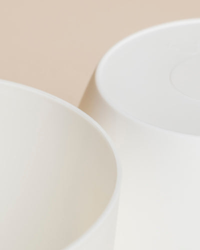 Nahaufnahme zweier weißer, glatter Kunststoff-Töpfe (Kiki | 11 cm Ø) auf neutralem, beigem Hintergrund, teilweise überlappend, mit weichen, minimalistischen Lichtakzenten für dein Zuhause.