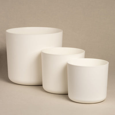 Drei weiße Töpfe des Topfsets „Lumi“ aus Kunststoff, die ein schlichtes Design aufweisen, sind vor einem neutralen beigen Hintergrund angeordnet. Diese minimalistischen Blumentöpfe sind in absteigender Reihenfolge von links nach rechts angeordnet und erzeugen eine ruhige und elegante visuelle Harmonie.