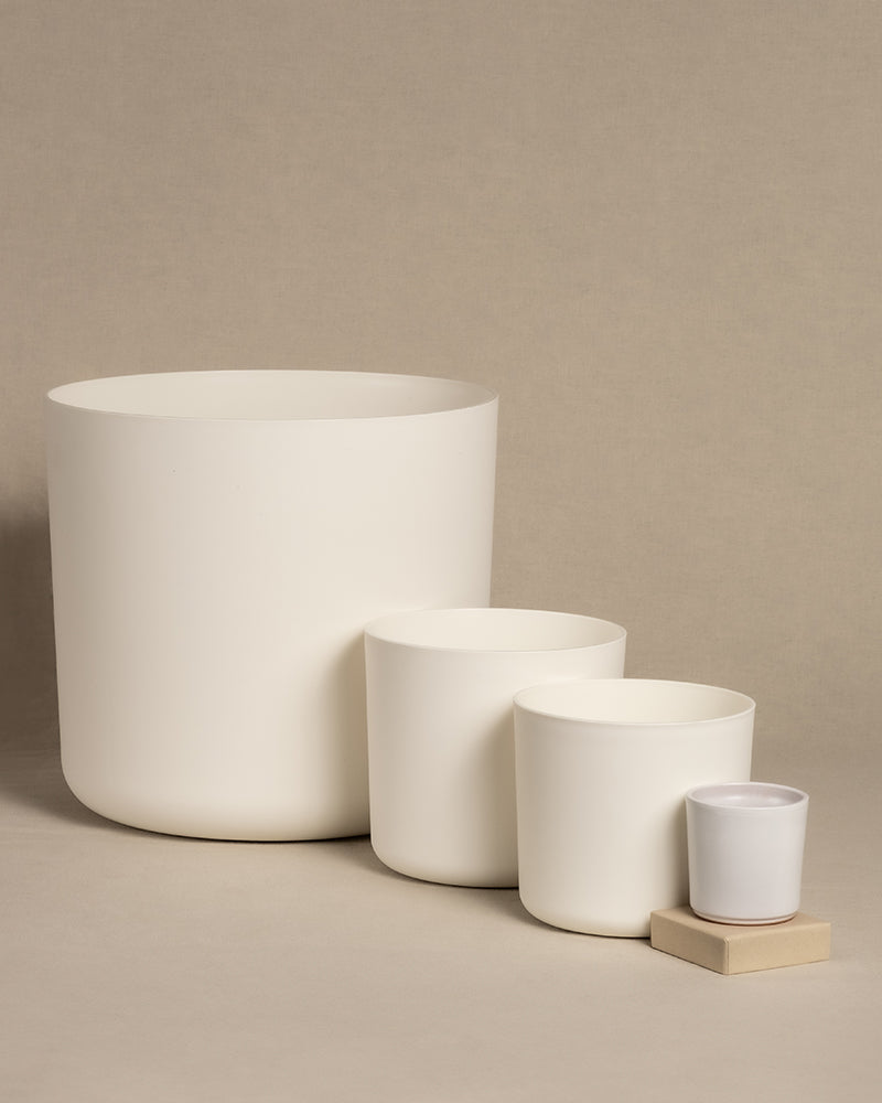 Ein Set aus vier Kunststofftöpfen der Kollektion „Lumi“ mit schlichtem Design aus weißer Keramik ist in absteigender Reihenfolge angeordnet. Der größte Topf (30) steht links, der kleinste (7) rechts und ruht elegant auf einem kleinen Holzblock vor einem neutralen Hintergrund.