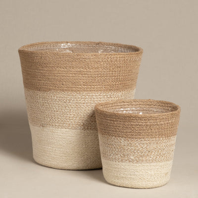 Zwei Pflanzenkorb-Set aus Jute (Lapis | 25, 16) Körbe in Naturtönen stehen nebeneinander, jeweils rund mit einem sanften Farbverlauf von beiger Oberseite nach weißer Unterseite; der größere Korb wird hinter dem kleineren platziert.