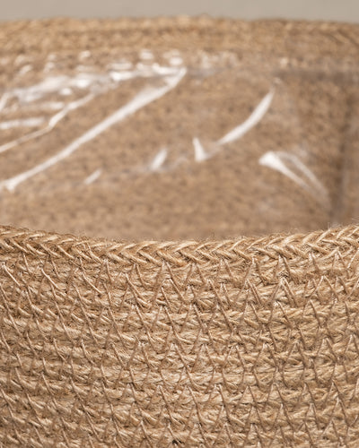 Nahaufnahme eines Korbs aus Naturfasern. Der handgemachte Pflanzenkorb aus Jute (Lapis | 22 cm Ø) weist ein Zickzackmuster und eine transparente Kunststoffauskleidung auf. Seine beige Farbe verleiht rustikalen Charme und ist ideal, um jede Zimmerpflanzenkorb-Ausstellung aufzuwerten.