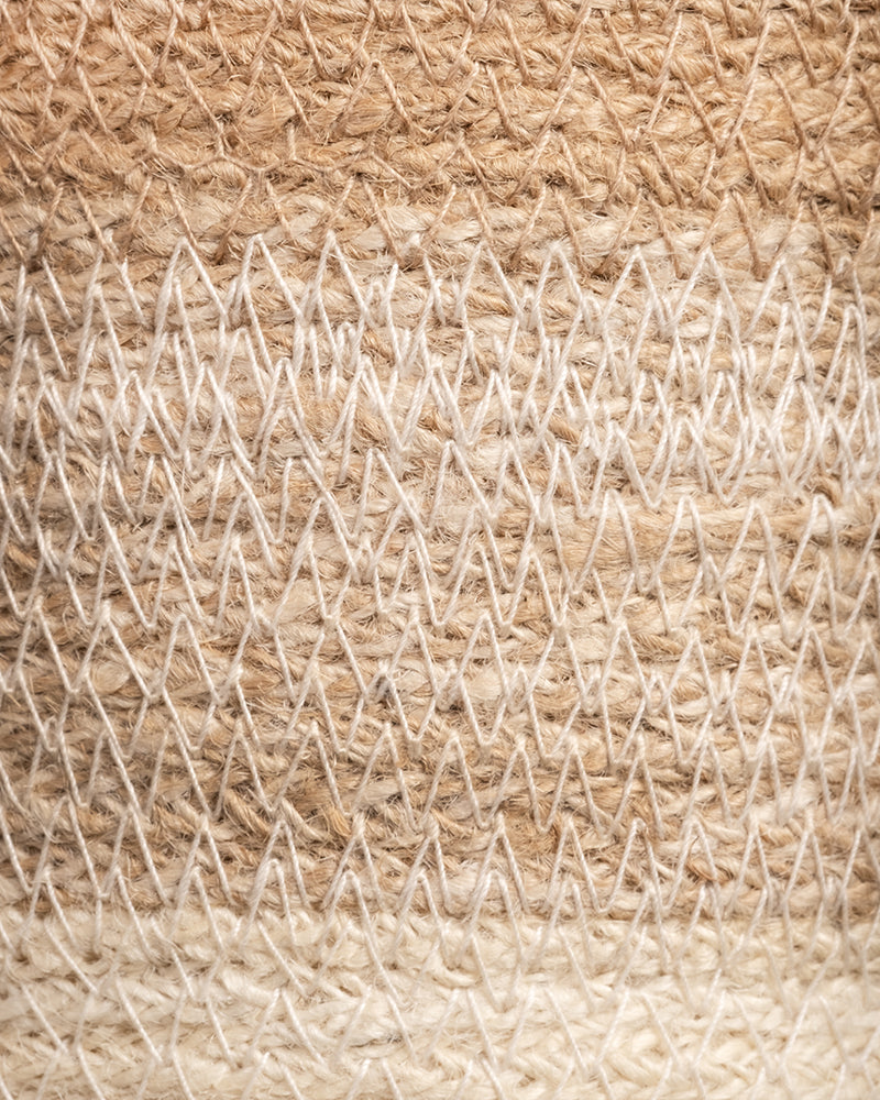 Nahaufnahme eines gewebten Textils mit Zickzackmuster in Beige- und Cremetönen, das an die Textur des Pflanzenkorbs aus Jute (Lapis | 22 cm Ø) erinnert. Die groben Fasern erzeugen ein komplexes Aussehen, wobei helle und dunkle Farbtöne Tiefe verleihen.