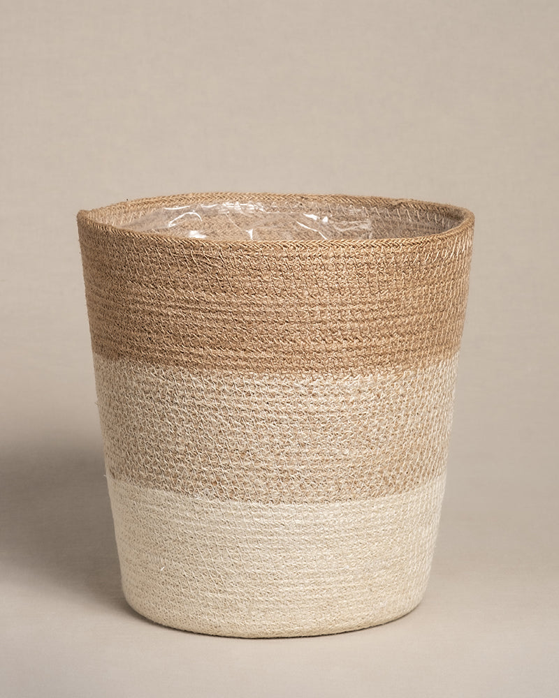 Der Pflanzenkorb aus Jute (Lapis | 25 cm Ø) besticht durch sein handgewebtes, zweifarbiges Design in Hellbraun und Creme. Er ist aus Jute gefertigt, hat eine zylindrische Form und ein dezentes Muster. Sein wasserdichtes Inneres ist mit einer transparenten Kunststoffauskleidung auf neutralem Beige ausgestattet.