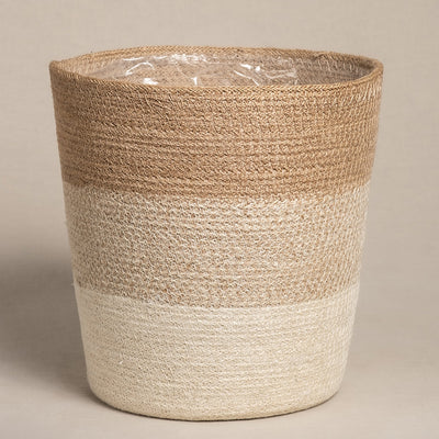 Der Pflanzenkorb aus Jute (Lapis | 25 cm Ø) ist ein handgefertigter Jutekorb in zylindrischer Form mit zwei horizontalen Bändern. Die obere Hälfte ist beige, die untere cremefarben und harmoniert so mit dem neutralen beigen Untergrund.