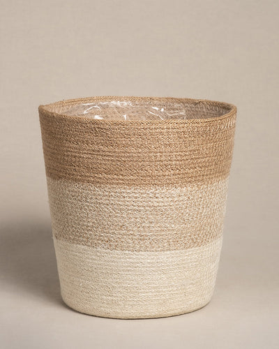 Der Pflanzenkorb aus Jute (Lapis | 25 cm Ø) besticht durch sein handgewebtes, zweifarbiges Design in Hellbraun und Creme. Er ist aus Jute gefertigt, hat eine zylindrische Form und ein dezentes Muster. Sein wasserdichtes Inneres ist mit einer transparenten Kunststoffauskleidung auf neutralem Beige ausgestattet.
