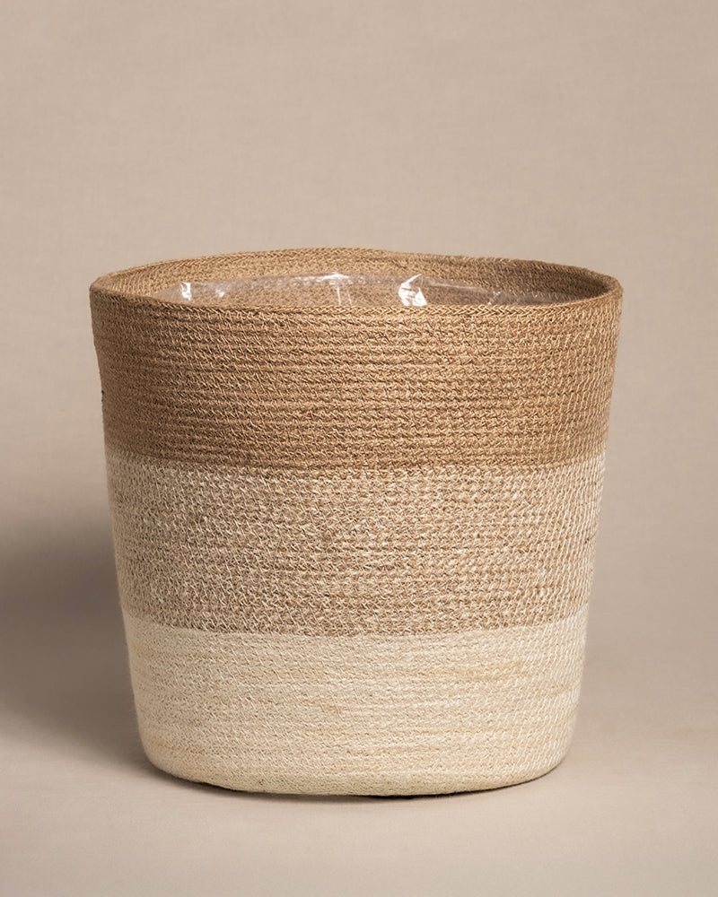 Der Pflanzkorb aus Jute (Lapis | 30 cm Ø) ist ein runder, handgefertigter Pflanzkorb mit zwei horizontalen Farbbändern: oben hellbraun und unten cremefarben. Er steht auf einer neutralen Oberfläche vor einem schlichten Hintergrund und verleiht jedem Raum Charme.