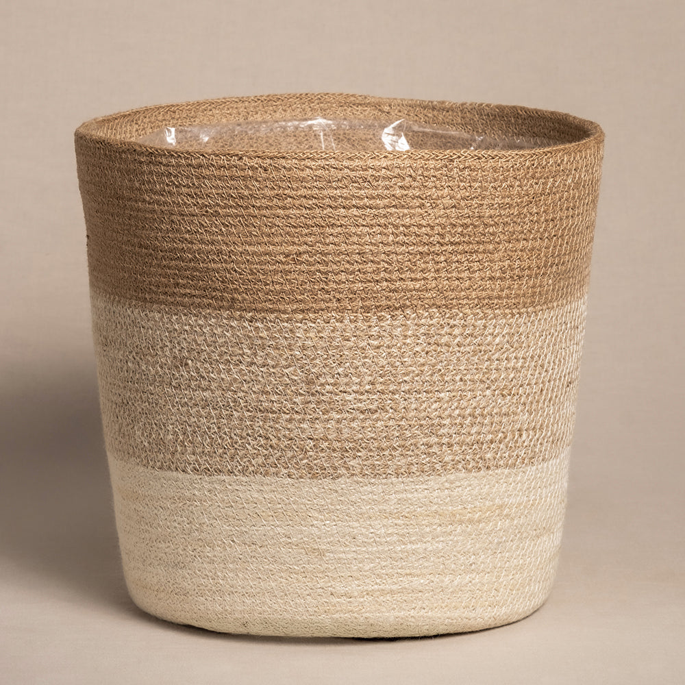 Der Pflanzkorb aus Jute (Lapis | 30 cm Ø) verfügt über ein rustikales, handgefertigtes Design mit einem Farbverlauf von hellem zu dunklem Beige, ergänzt durch einen wasserdichten Pflanzenkorb-Innenteil. Sein schlichter Charme vor einem neutralen Hintergrund macht ihn perfekt für jeden Garten.