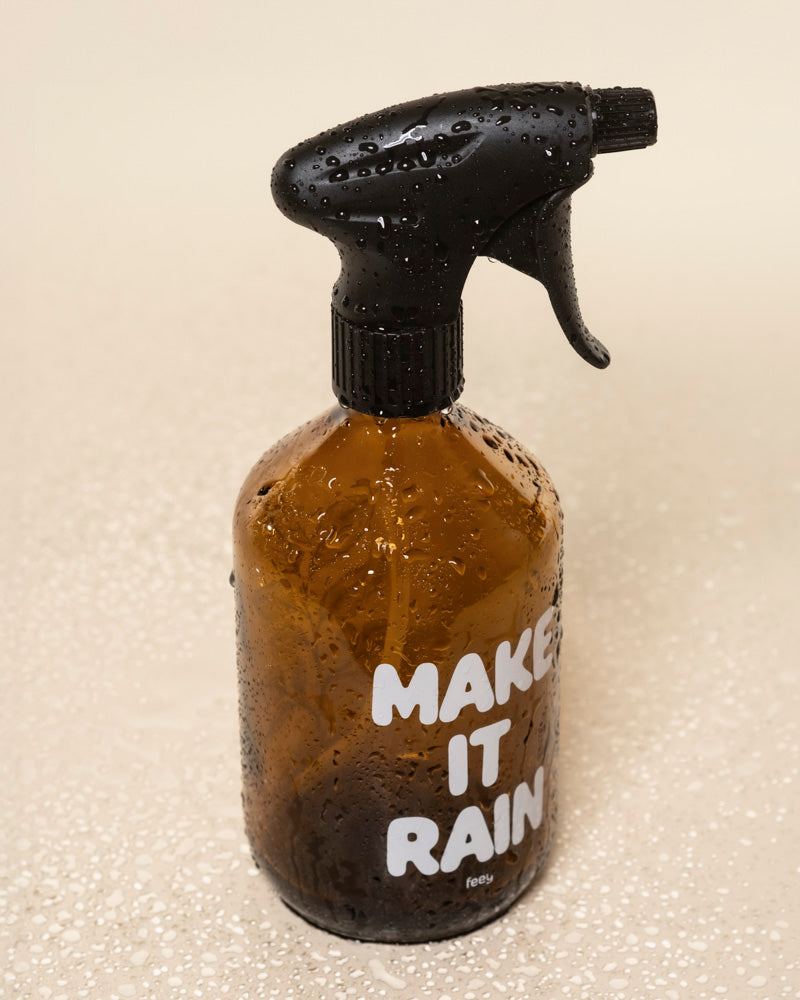 Ein brauner Pflanzensprüher mit schwarzer Düse und weißem "MAKE IT RAIN"-Schriftzug sitzt auf einer nassen, hellen Fläche. Seine Wassertropfen unterstreichen den perfekten Einsatz für die Pflege Ihrer Lieblingspflanzen.