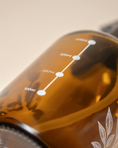 Nahaufnahme der Pflanzensprher-Flasche aus braunem Glas mit klarer weißer Milliliter-Markierung (100ml-400ml) und botanischem Motiv am Boden - ideal für die Pflege Ihrer Pflanzen.