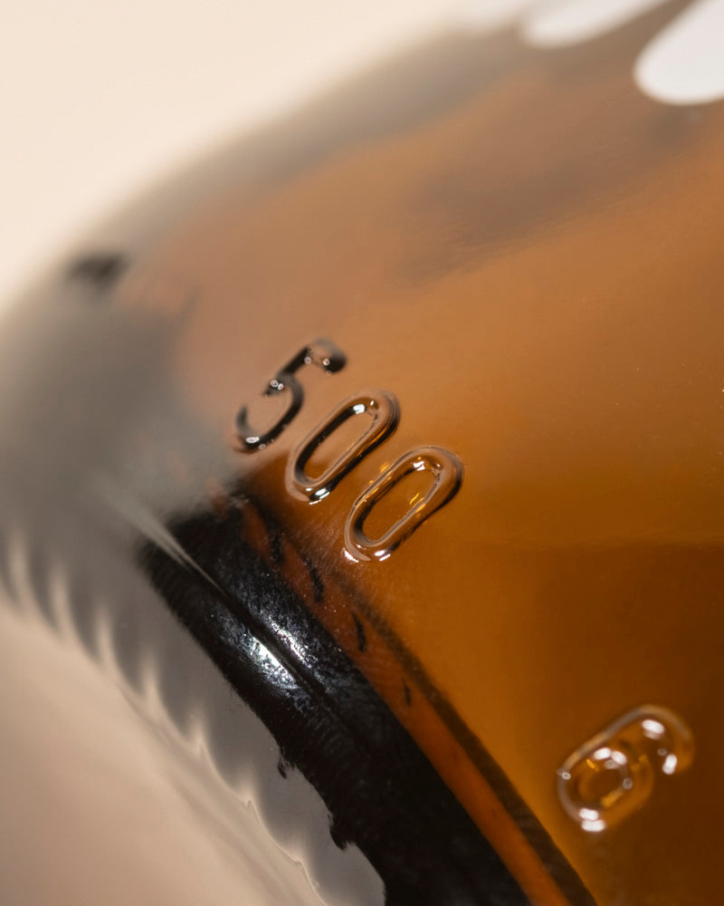 Nahaufnahme einer bernsteinfarbenen Pflanzensprher-Flasche mit der erhabenen Markierung "500" für das Fassungsvermögen. Ihre glänzende Oberfläche reflektiert das Licht mit sanft verschwommenen Rändern - ideal zum Gießen und Pflegen Ihrer Pflanzen.