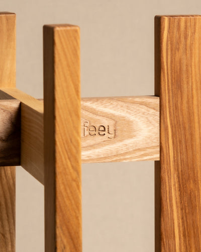 Nahaufnahme eines Holzmöbelstücks aus Eschenholz mit dem eingravierten Wort „feyy“. Die natürliche Oberfläche bringt Maserung und Struktur zur Geltung und erinnert an einen edlen Pflanzenständer (Stelion | 22 cm Ø). Der sanft verschwommene Hintergrund unterstreicht die exquisite Handwerkskunst.