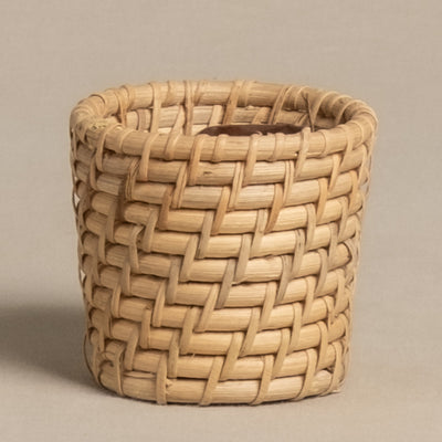 Der Rattan Babypflanzen-Korb 'Calen' ist ein kleiner, zylindrischer Korb aus hellem Rattan mit dickem, abgerundetem Rand und fester Webstruktur, präsentiert vor schlicht beigem Hintergrund.