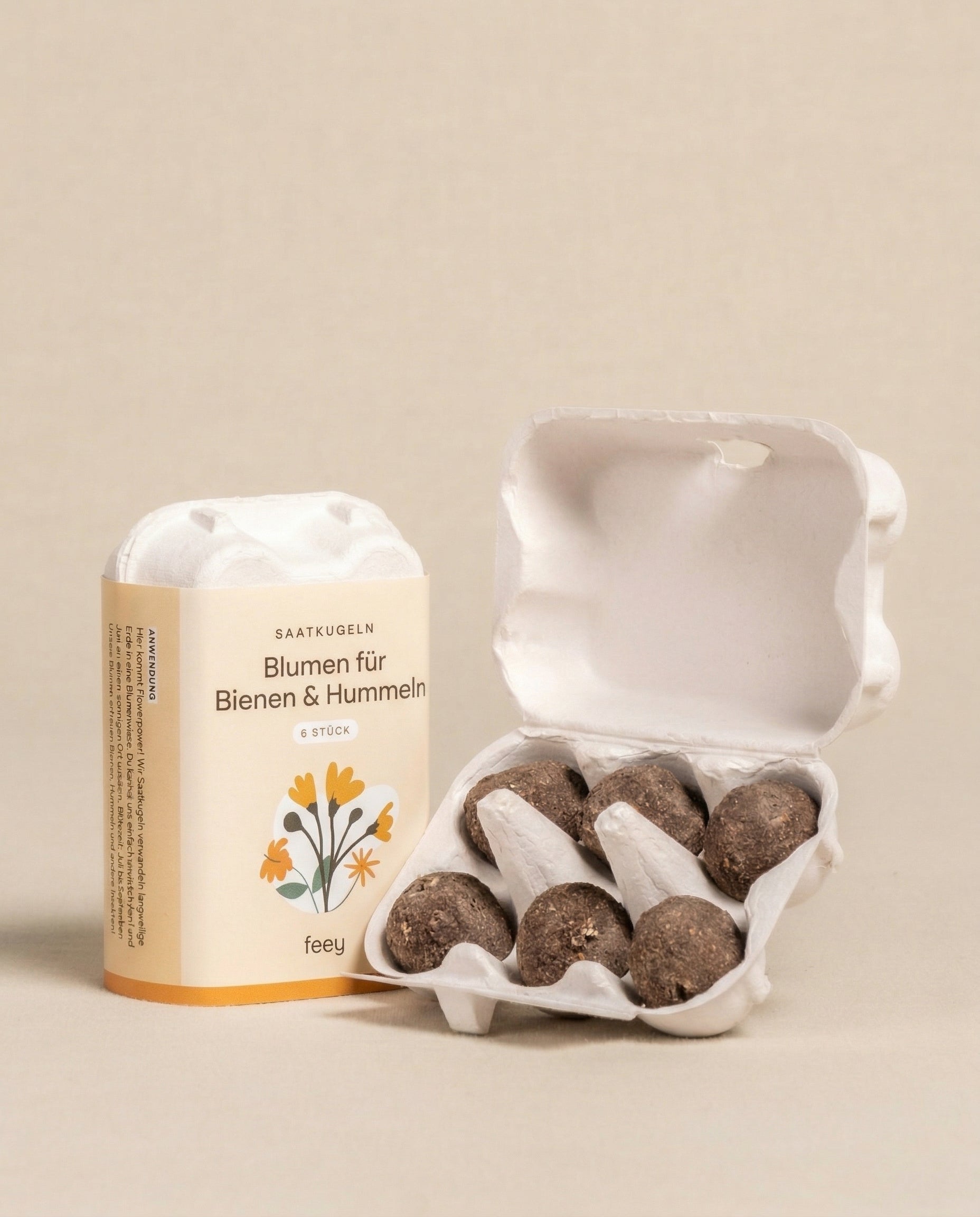 Ein kleiner offener Karton enthält sechs runde Saatkugeln für Feld- & Wiesenblumen, deren Verpackung mit 