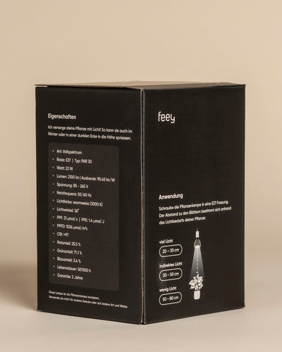 Ein schwarzer Kasten mit weißem Text und dem Markennamen "feey" zeigt die deutschen Spezifikationen der Pflanzenlampe - Wattleistung, sonnenähnliches Spektrum und Installationshinweise. Eine Illustration zeigt, wie die Lampe Zimmerpflanzen beleuchtet.