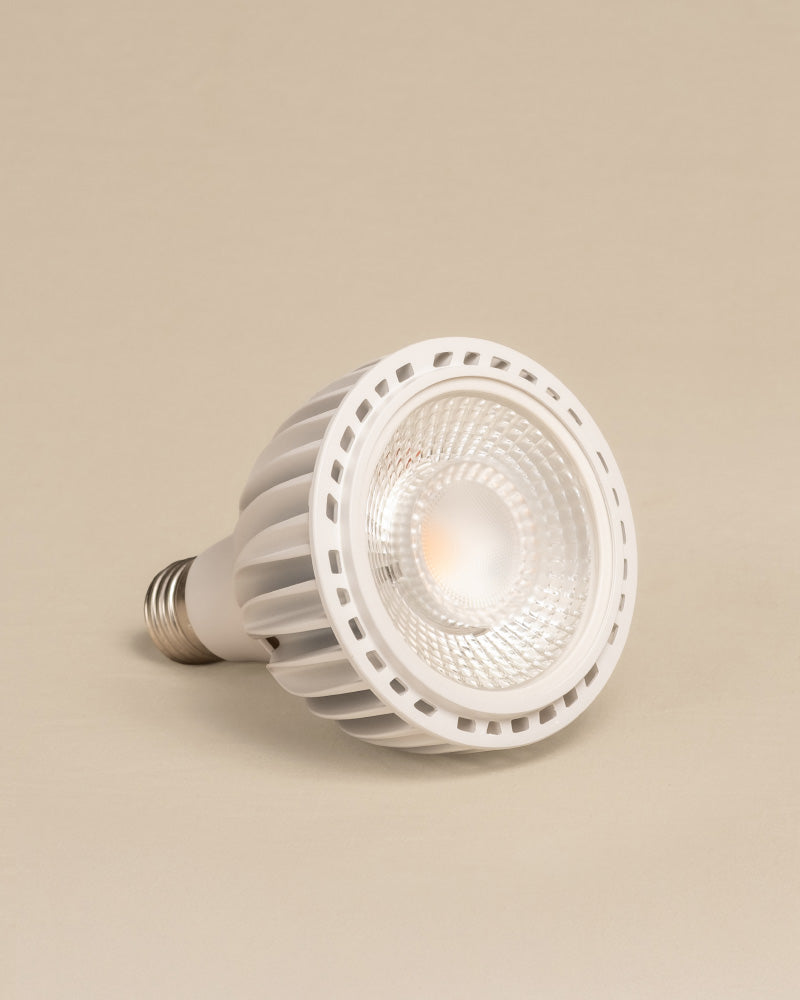 Eine weiße Pflanzenlampe mit metallischem Schraubsockel ruht auf der Seite vor einem beigen Hintergrund. Mit ihrer strukturierten Linse und dem belüfteten Kühlkörper ist sie perfekt für die Versorgung von Zimmerpflanzen mit Sonnenlicht geeignet.