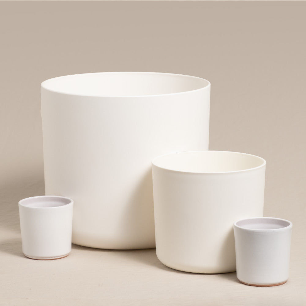 Ein Foto von vier weißen Kunststoff-Topfsets „Lumi“ (22, 14, 2× 7) in verschiedenen Größen aus Keramik vor einem neutralen Hintergrund. Die Pflanzgefäße sind so angeordnet, dass zwei große hinten und zwei kleinere vorne stehen. Die kleinsten Pflanzgefäße haben einen leicht bräunlichen Boden, was ihnen einen sencillo-Look verleiht.