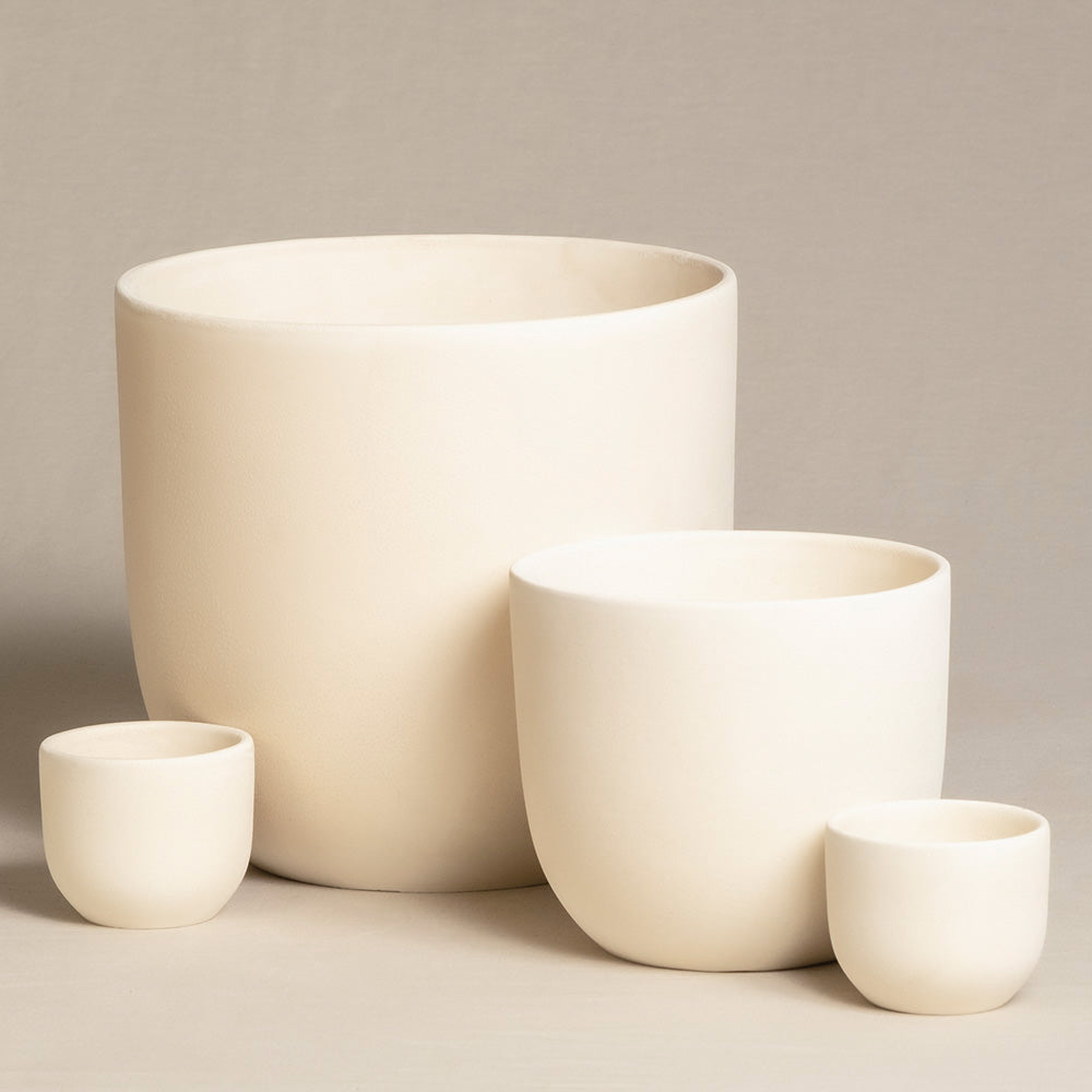 Eine Nahaufnahme von vier handgefertigten, minimalistischen Keramiktöpfen unterschiedlicher Größe. Das Keramik-Topfset „Direito“ (22, 14, 2 × 7) ist auf einer neutralen, beigen Oberfläche mit beigem Hintergrund angeordnet und zeigt seine glatte Textur und sein einfaches, zylindrisches Design – perfekt für Zimmerpflanzen.