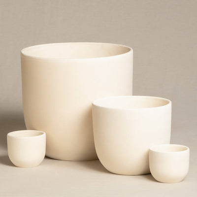 Eine Nahaufnahme von vier handgefertigten, minimalistischen Keramiktöpfen unterschiedlicher Größe. Das Keramik-Topfset „Direito“ (22, 14, 2 × 7) ist auf einer neutralen, beigen Oberfläche mit beigem Hintergrund angeordnet und zeigt seine glatte Textur und sein einfaches, zylindrisches Design – perfekt für Zimmerpflanzen.
