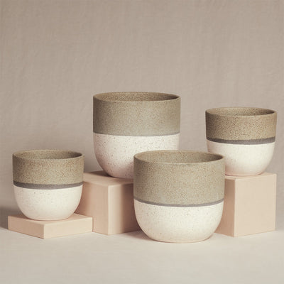 Ein Set aus vier handgefertigten, minimalistischen, runden Keramik-Pflanzgefäßen in verschiedenen Größen. Jedes Keramik-Topfset „Variado“ (2 × 18, 2 × 14) hat einen gesprenkelten, cremefarbenen Sockel mit einem hellbeigen Band an der Oberseite. Sie stehen auf hellrosa Sockeln vor einem beigen Hintergrund und eignen sich perfekt zur Präsentation Ihrer Zimmerpflanzen.