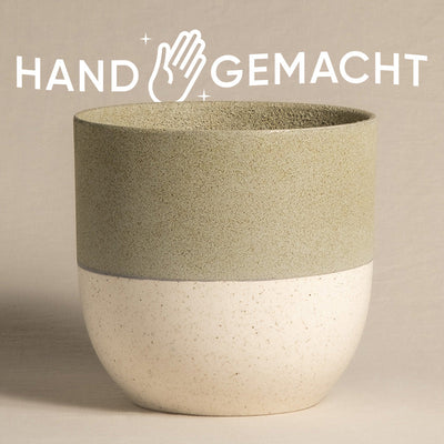 Ein schöner Keramik-Topf (Variado | 22 cm ⌀) aus der Topfkollektion Variado, mit einer rauen, strukturierten grünen oberen Hälfte und einer glatten, cremefarbenen unteren Hälfte. Über dem Topf steht in Großbuchstaben „HANDGEMACHT“ mit einem Handsymbol und funkelt zwischen „HAND“ und „GEMACHT“.